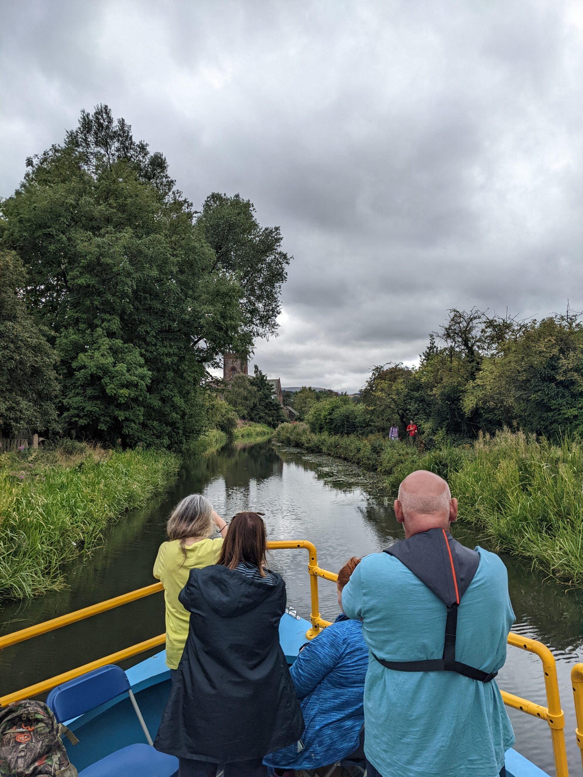 People on a canal boat with a view of the canal, trees and a church
